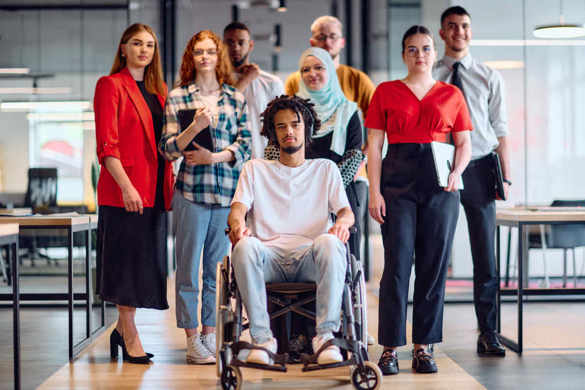 NDIS Community Participation - A diverse group of young business people walking a corridor in the glass-enclosed office of a modern