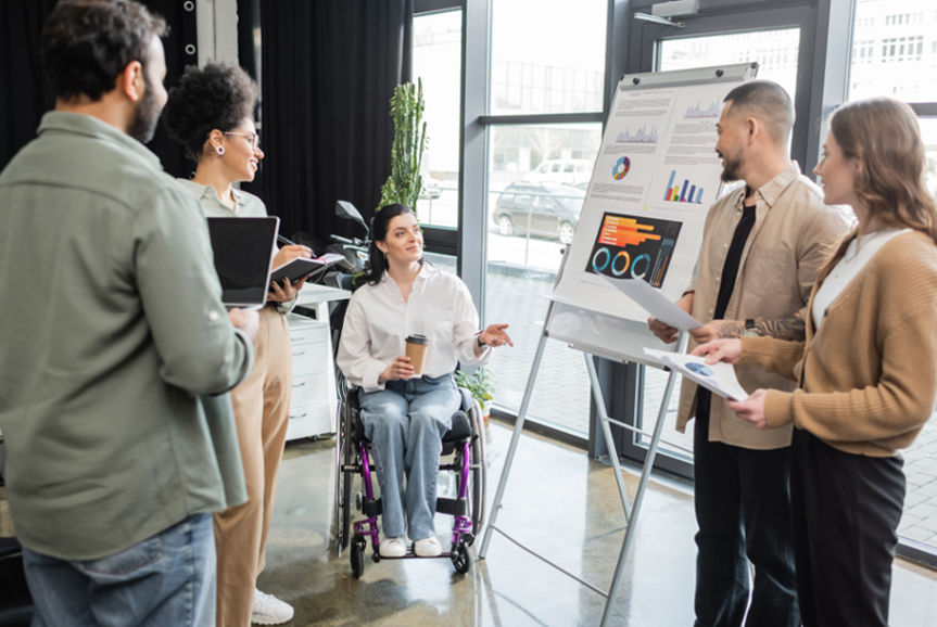 Increased Social and Community Participation Budget - inclusion concept, disabled woman in wheelchair sharing ideas with interracial startup team